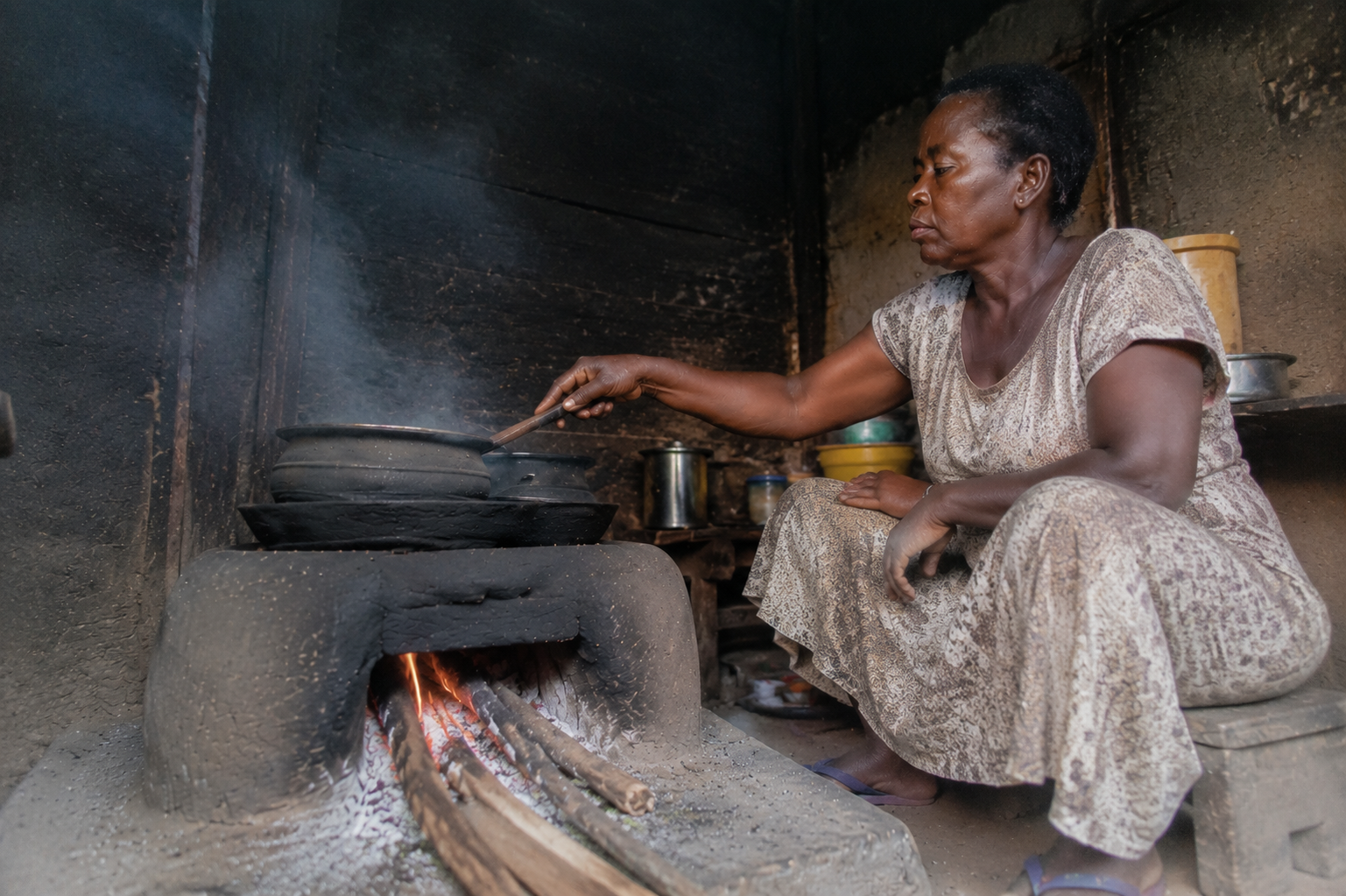 Why Now / Energy — smoke from a wood/charcoal cooking fire in a kitchen.